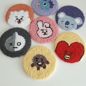 May include: Seven round, colorful, embroidered coasters featuring different cartoon characters. The coasters are made of a soft, fluffy material and are perfect for adding a touch of whimsy to any home.