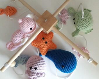 May include: A wooden baby mobile with crocheted sea creatures. The mobile features a pink octopus, a blue whale, a pink seahorse, an orange starfish, and a green crab.