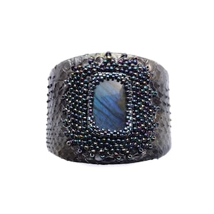 May include: A black leather cuff bracelet with a large iridescent blue gemstone surrounded by black beads.