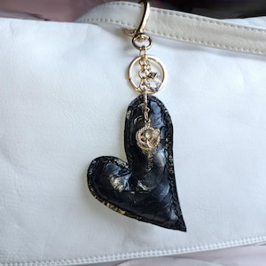 May include: A black leather heart-shaped keychain with a gold-tone chain and a small crystal charm.
