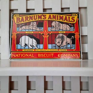 May include: Vintage metal sign featuring the text "BARNUM'S ANIMALS" with illustrations of a tiger, lion, polar bear, and bison. The sign has a red and yellow border and includes the text "NATIONAL BISCUIT COMPANY".