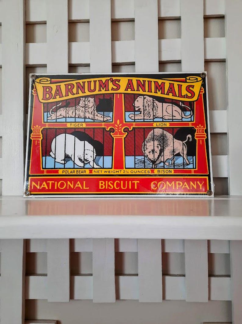 May include: Vintage metal sign featuring the text "BARNUM'S ANIMALS" with illustrations of a tiger, lion, polar bear, and bison. The sign has a red and yellow border and includes the text "NATIONAL BISCUIT COMPANY".
