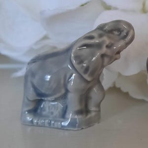May include: A small, gray ceramic elephant figurine with a textured surface. The figurine is standing on a base with the word "Enesco" printed on it.