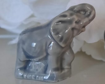 May include: A small, gray ceramic elephant figurine with a textured surface. The figurine is standing on a base with the word "Enesco" printed on it.