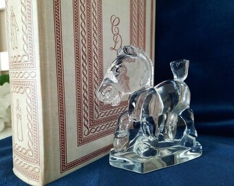 May include: A clear glass figurine of a horse with a raised tail and a base. The figurine is on a blue surface.