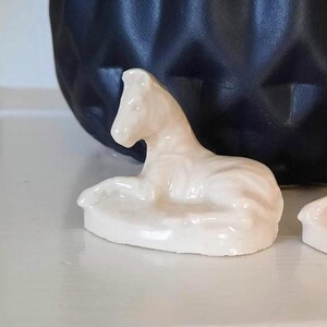 May include: A white ceramic figurine of a zebra lying down. The figurine is detailed with a textured surface and is a small, decorative piece.