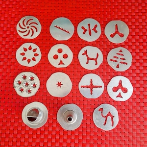 May include: A collection of silver cookie cutters in various shapes, including a spiral, star, dog, and tree. The cutters are arranged on a red woven surface, showcasing their diverse designs and potential for baking. The image highlights the variety of shapes available.