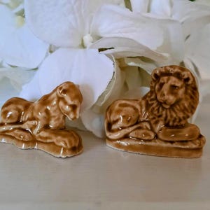 May include: Two small ceramic figurines of a lion and a panther, both lying down. The figurines are brown and have a textured surface.