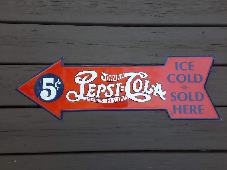 May include: Vintage Pepsi-Cola arrow-shaped sign. The sign is red with white and blue lettering. It reads "Drink Pepsi-Cola" and "Ice Cold Sold Here." The sign also features the price "5&cent;".