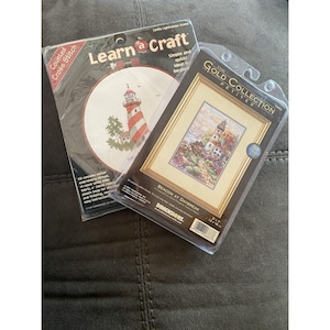 Könnte beinhalten: Zwei Zählkreuzstich-Sets von Dimensions. Eines ist ein Learn a Craft-Set mit einem Leuchtturmmotiv und einem 15 cm Stickrahmen. Das andere ist ein Gold Collection Petites-Set namens Beacon at Daybreak mit einem 13 cm mal 18 cm großen Motiv.