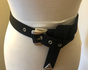 May include: A black fabric belt with a silver buckle. The belt is designed to be worn with the buckle on the side and the strap crossing over the front.