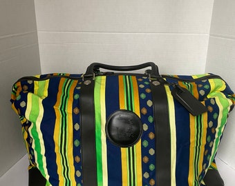 Puede incluir: Una gran bolsa de viaje a rayas con detalles de cuero negro y un logotipo circular. La bolsa está hecha de una tela colorida con rayas azules, amarillas, verdes y marrones. La bolsa tiene dos asas superiores y un cierre de cremallera.