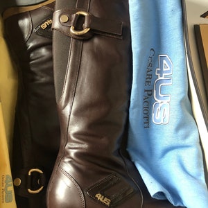 May include: Brown leather knee-high boots with a gold buckle and a black and gold logo that says "4US Cesare Paciotti".
