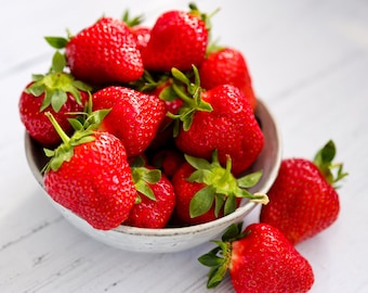 May include: A white bowl filled with fresh, red strawberries. The strawberries are arranged in a cluster, with some spilling over the edge of the bowl.