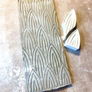 May include: A gray textured rectangular silicone mold with a repeating pattern of arched leaves. Two smaller white silicone molds with the same leaf pattern are also shown.