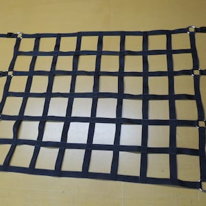 May include: Black cargo net with metal rings and adjustable straps. The net is made of thick, durable webbing and is designed to secure items in a truck bed or other cargo area.