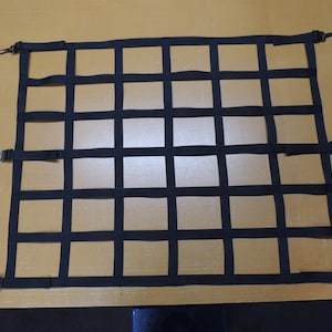 May include: Black cargo net with metal hooks. The net is made of thick black webbing and has a grid pattern. The net is designed to secure items in a truck bed or other cargo area.