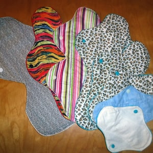 May include: A set of six reusable cloth menstrual pads in various patterns and colors, including gray, black, white, blue, green, and pink. The pads are made of soft, absorbent fabric and are designed to be comfortable and discreet.