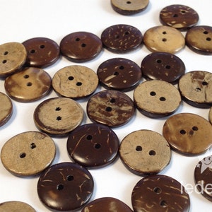 Könnte beinhalten: Eine Sammlung von braunen und beigefarbenen Kokosnuss-Knöpfen mit jeweils zwei Löchern. Die Knöpfe sind auf einer weißen Oberfläche verstreut.