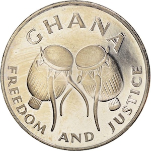 May include: A silver coin featuring the word "GHANA" at the top and the words "FREEDOM AND JUSTICE" around the edge. Two stylized drums are in the center. The coin has a shiny, reflective surface.