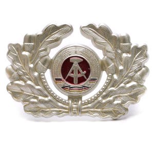 May include: Silver metal badge with a red circle containing a compass and hammer, surrounded by a wreath of oak leaves.