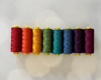 May include: A row of eight spools of thread in a rainbow of colors. The colors include red, orange, yellow, green, teal, blue, purple, and burgundy. Each spool has a yellow label.