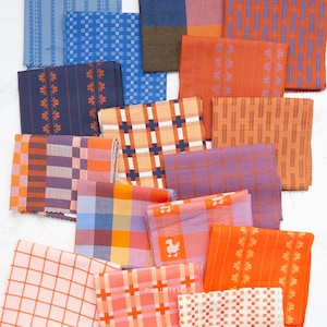 May include: A collection of folded fabric swatches featuring various patterns including plaids, checks, and floral stripes in a vibrant color palette of orange, blue, purple, and pink. The textiles display diverse geometric and botanical motifs.