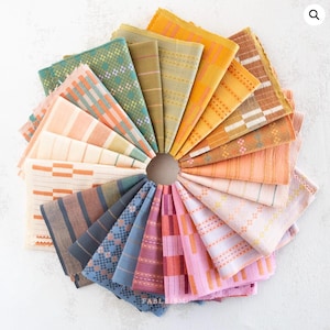 May include: A circular arrangement of folded fabric squares in various patterns and colours. The squares feature stripes, checks, and geometric designs. The colour palette includes muted greens, blues, warm oranges, and pinks. The word "FABLEISM" is visible.