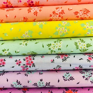 May include: A stack of fabric rolls in various colors, including pink, peach, yellow, green, light blue, and lavender. Each roll is printed with a floral pattern featuring white and pink flowers with green leaves. The fabric appears to be cotton.