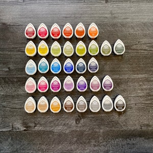 May include: A collection of 36 ink pads in various colours, arranged in a triangular pattern. Each pad is labelled "Memento" and features a teardrop shape.