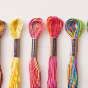May include: Six spools of colourful embroidery floss, each with a label that reads "Seasons". The floss is arranged in a row, with the colours ranging from purple and green to yellow and red.
