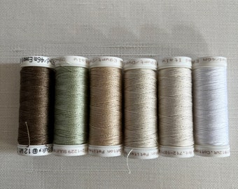 May include: A row of six spools of thread in various neutral colors, including brown, green, beige, and white. The spools are labeled with text indicating the thread type and length, with each spool containing approximately 50 yards of thread.