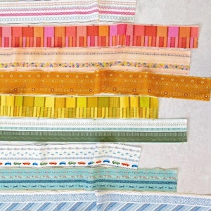 May include: A collection of colorful fabric ribbons in various patterns and designs. The ribbons include floral, geometric, and striped patterns in shades of pink, orange, yellow, green, and blue. The ribbons are arranged in a layered, overlapping fashion.