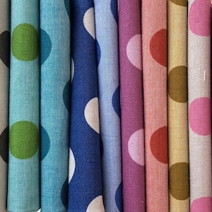 May include: A collection of rolled fabric samples in various colors, each featuring a large polka dot design. Colors include teal, blue, pink, and burgundy, with white and brown dots. The fabric has a textured appearance.
