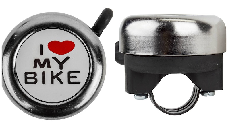 May include: A silver bicycle bell with a black lever and mounting bracket. The bell face has a white background with a red heart and the words "I MY BIKE" in black.