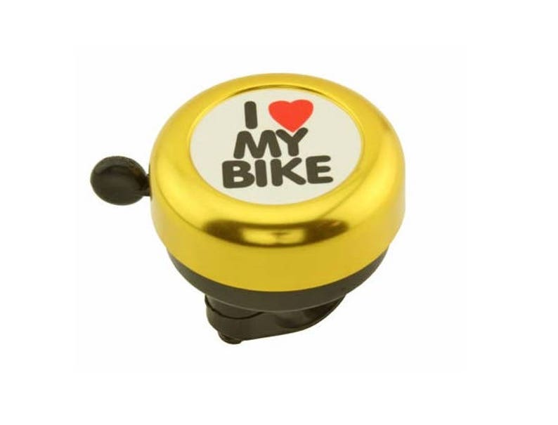 May include: A gold-colored bicycle bell with a black lever. The bell has a white center with the words "I MY BIKE" and a red heart symbol. The bell is designed to attach to a bicycle handlebar.