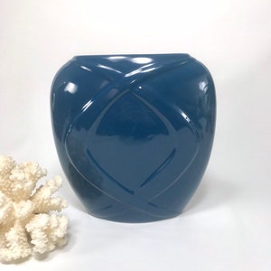 May include: A glossy, navy blue ceramic vase with a geometric, quilted pattern. The vase has a rounded shape and a wide opening. A piece of white coral is in the background.