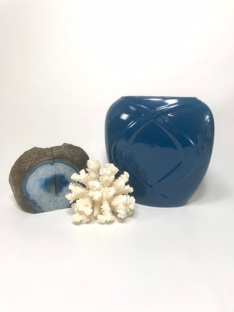 May include: A still life arrangement featuring a blue vase with a geometric design, a piece of white coral, and a blue and brown geode. The objects are arranged on a white surface.