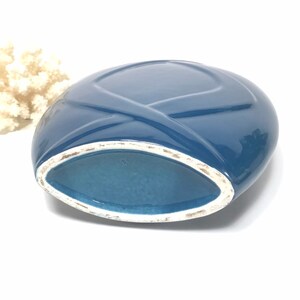 May include: A blue ceramic vase with a unique oval shape and a crisscross design on the top. The interior is a lighter shade of blue, and the rim has a white trim. The vase is likely a decorative item.