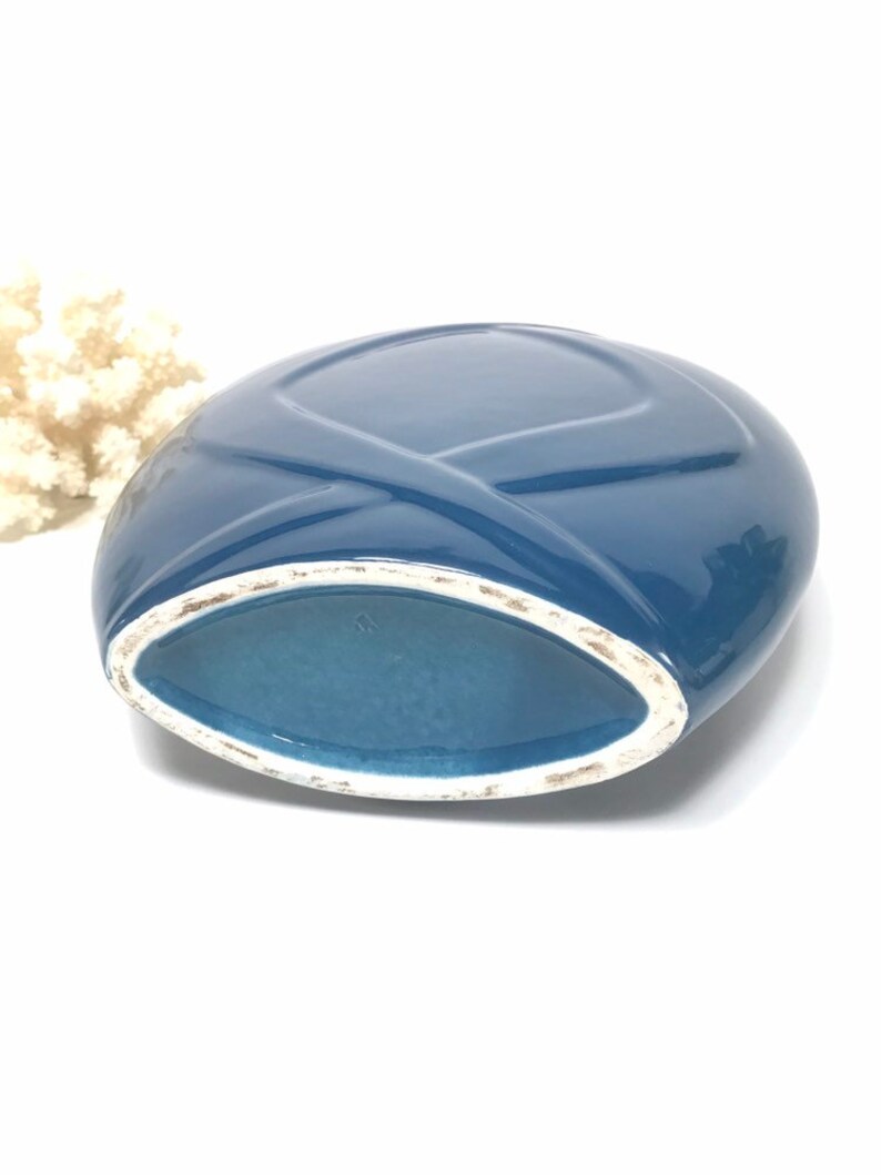 May include: A blue ceramic vase with a unique oval shape and a crisscross design on the top. The interior is a lighter shade of blue, and the rim has a white trim. The vase is likely a decorative item.