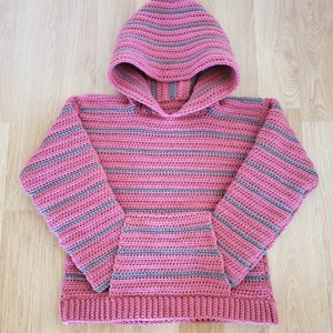 May include: A pink and gray striped crocheted hooded sweater with a pocket. The sweater has a hood with a pointed top and a ribbed hem.