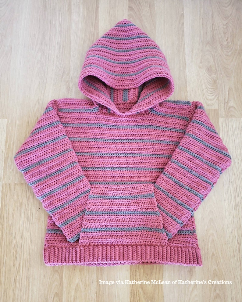 May include: A pink and gray striped crocheted hooded sweater with a pocket. The sweater has a hood with a pointed top and a ribbed hem.