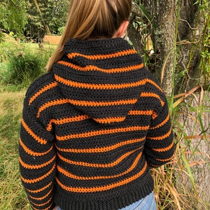 May include: A black and orange striped crocheted hooded sweater with long sleeves.