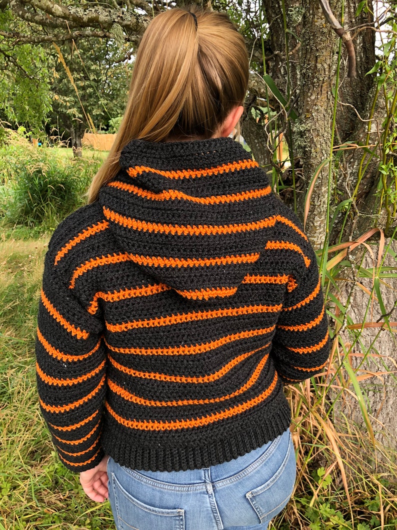 May include: A black and orange striped crocheted hooded sweater with long sleeves.