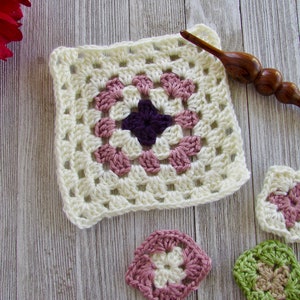 May include: A white crochet granny square with a pink and purple center. There are three smaller crochet squares in pink, green, and white.