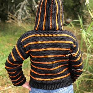 May include: A black and orange striped crocheted hooded sweater with long sleeves.