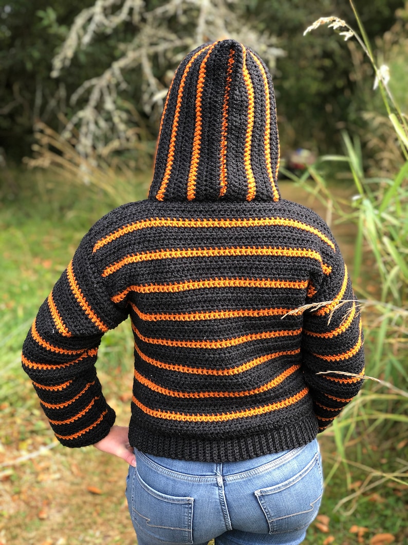 May include: A black and orange striped crocheted hooded sweater with long sleeves.