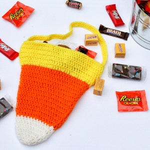 May include: A crocheted candy corn bag with a white, orange, and yellow design. The bag is filled with various candy bars and chocolate.