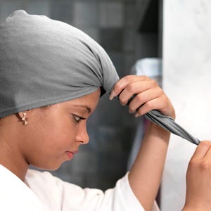 May include: A person is wrapping a grey satin hair wrap around their head. The hair wrap is designed to help keep hair smooth and frizz-free.