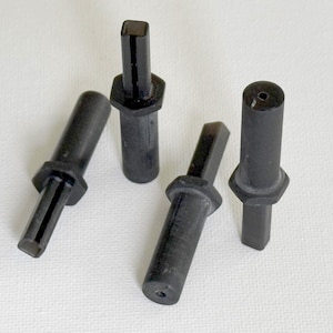 May include: Four black, cylindrical objects with a square top and a hexagonal base. The objects are arranged on a white surface. The objects appear to be made of a solid, dark material.